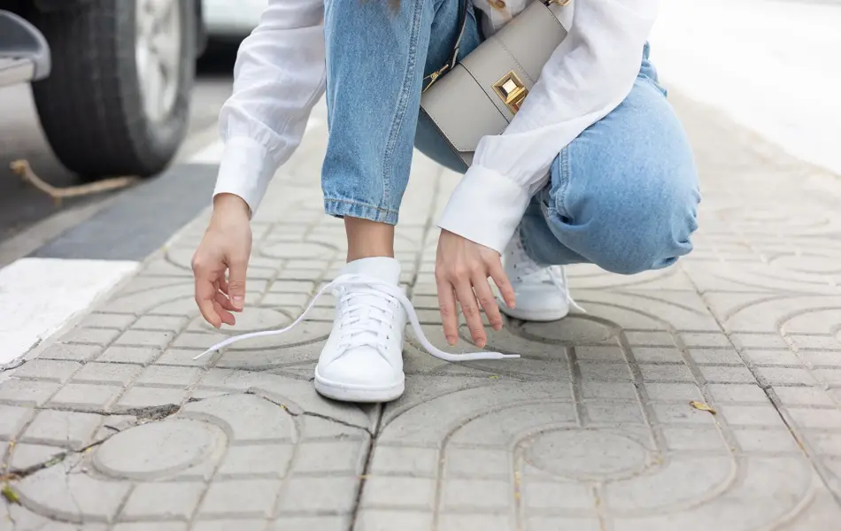 Nærbilde av damehender som knyter lisser på hvite sneakers på fortau 