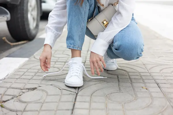 Nærbilde av damehender som knyter lisser på hvite sneakers på fortau 