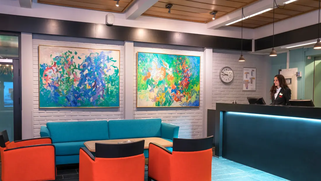 Betjent resepsjon med sofa og sitteplasser og store abstrakte bilder på veggen med dus belysning på Thon Hotel Skeikampen
