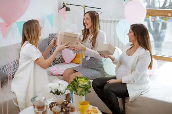 Three cheerful pregnant women exchanging gifts on baby shower