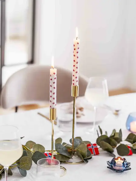 Bord dekket med hvit duk, to lysestaker i gull med stearinlys med flagg, grønne grener og flagglenke som bordpynt, telysholdere, vinglass.