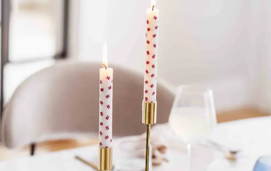 Bord dekket med hvit duk, to lysestaker i gull med stearinlys med flagg, grønne grener og flagglenke som bordpynt, telysholdere, vinglass.