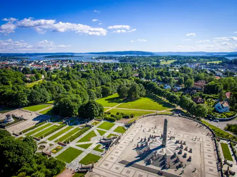 Monolith Statue photographed from the air, using a drone. 
In the horizon the Inner Oslofjord can be seen and the clear blue sky of June is in the background.

Monolith is a stone statue placed on "Monolith Plateau" in Vigeland Park in Oslo.  It consists of 121 figures. The sculpture is surrounded by a circular staircase with 36 groups of figures in granite arranged in rows up the stairs. The sculpture is carved out of a single granite block.