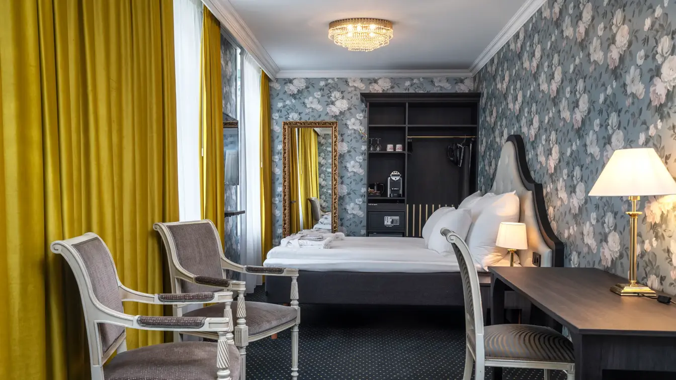 Tapetvegg, dobbeltseng, tre stoler, skrivebord, vindu, gule gardiner, skap 