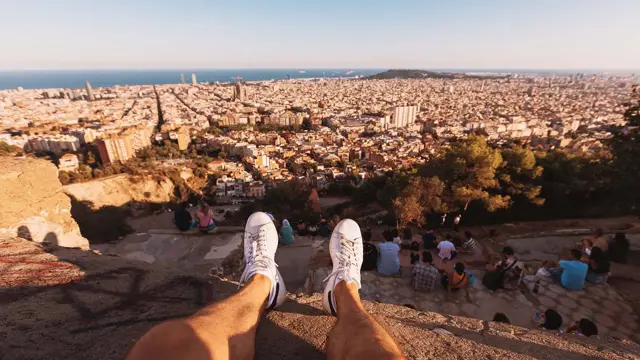 Mann sitter på en klippe. Man ser bena hans i lufta. Nedenfor er Barcelona.