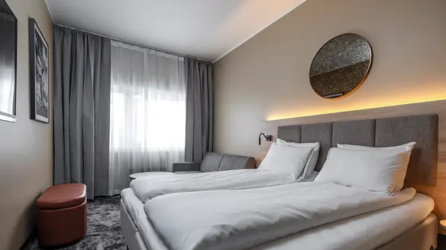 Dobbeltrom med dobbeltseng, sofa, puff, vegghengt TV, grå og hvite gardiner.