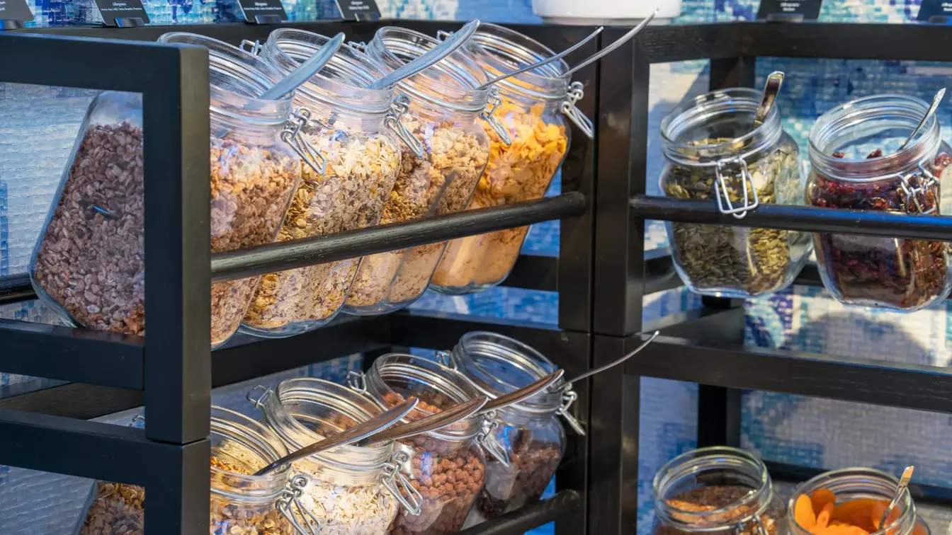 Nærbilde av krukker med granola og müsli i hylle på frokostbuffet ved Thon Hotel Skis frokostsal