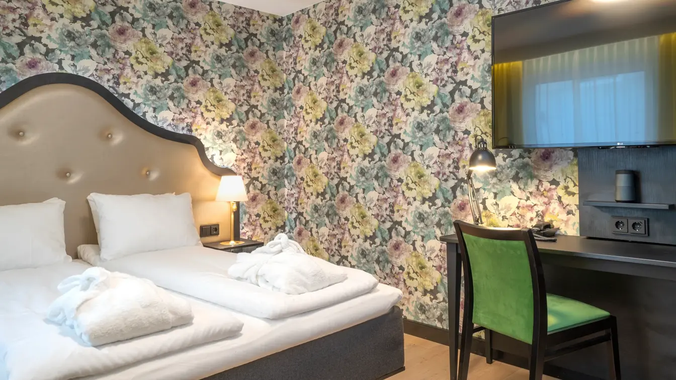 Blomstret tapet og dobbeltseng i dobbeltrom, gule gardiner, tv og arbeidsplass på Thon Hotel Cecil i Oslo sentrum