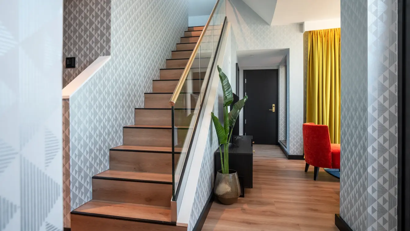 Trapp opp i andre etasje, gule gardiner, rød stol, tapetgulv, vindu