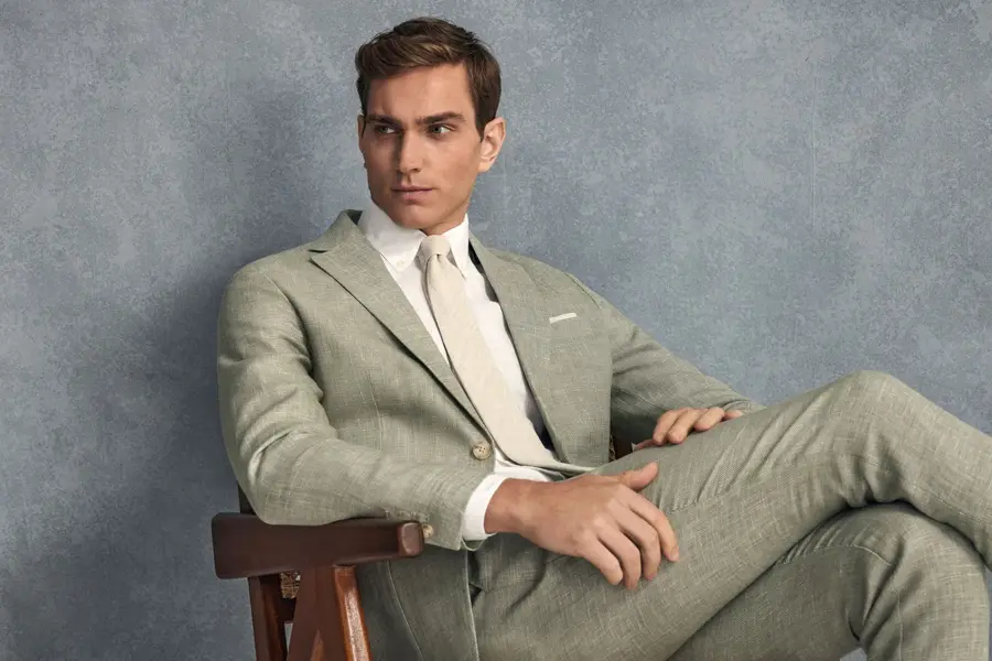 Velkledt mann sitter med bena i kors i en lys grønn lin-kjole med en hvit skjorte og lys beige slips