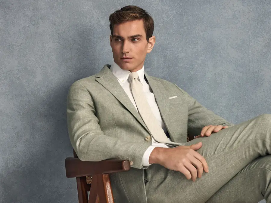 Velkledt mann sitter med bena i kors i en lys grønn lin-kjole med en hvit skjorte og lys beige slips