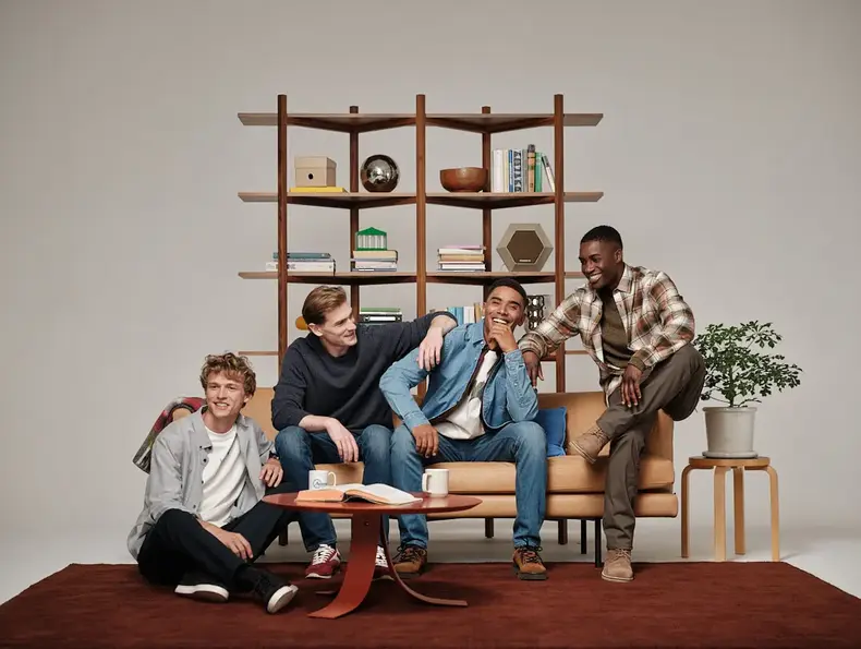 Fire menn sitter på en beige sofa og ler sammen.
