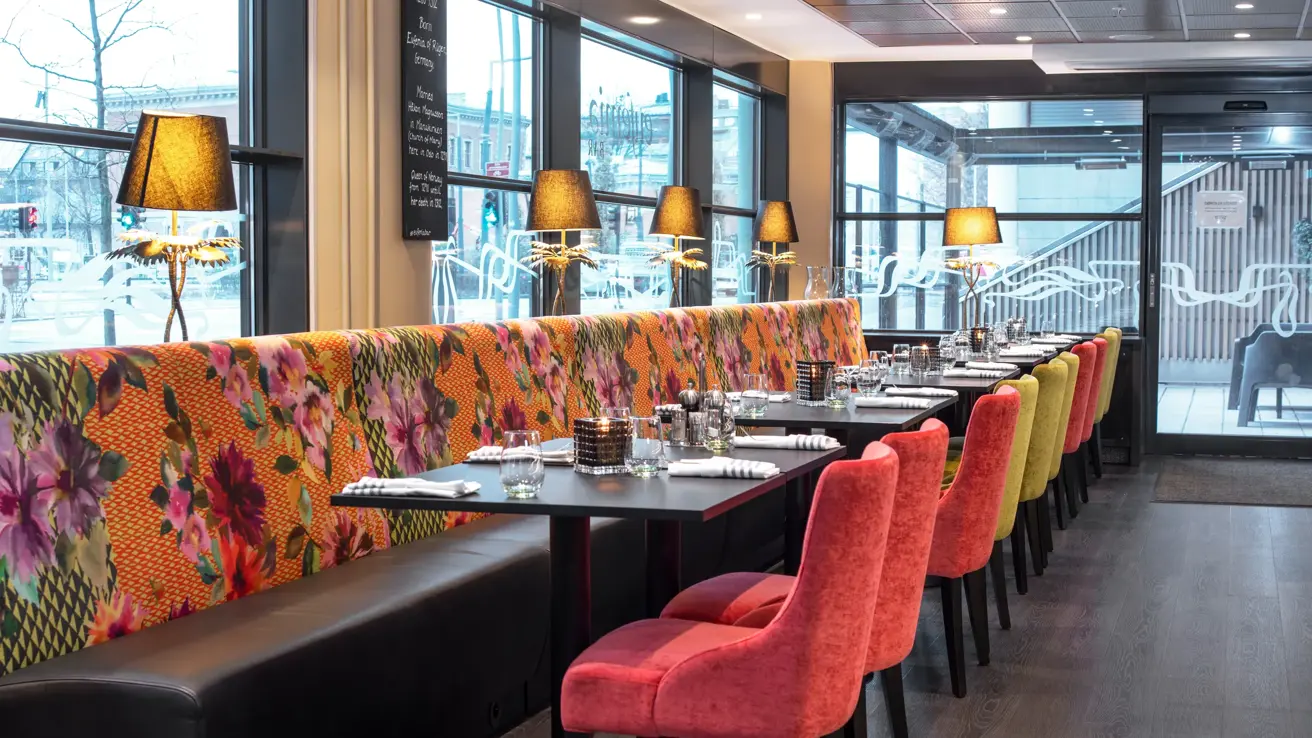 Svarte bord, vindu, rosa og grønne stoler, lamper.