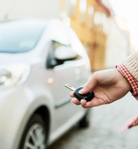 En hånd som holder en bilnøkkel foran en hvit bil