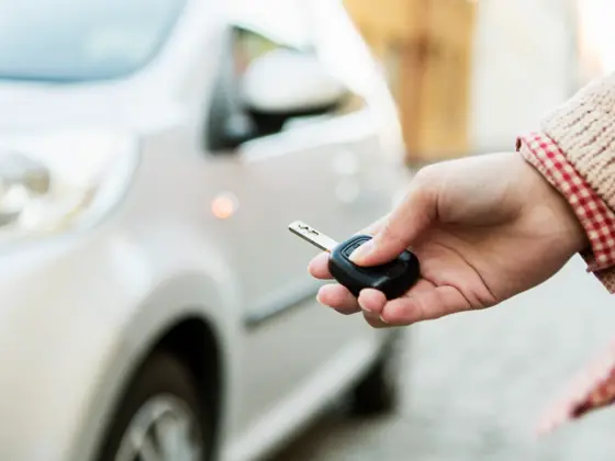 En hånd som holder en bilnøkkel foran en hvit bil