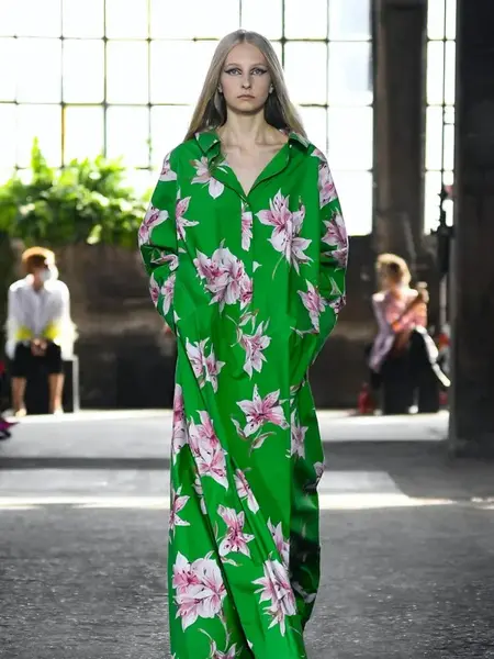 Dame som går på catwalken med lang grønn fotsid kjole med store rosa og hvite blomster på