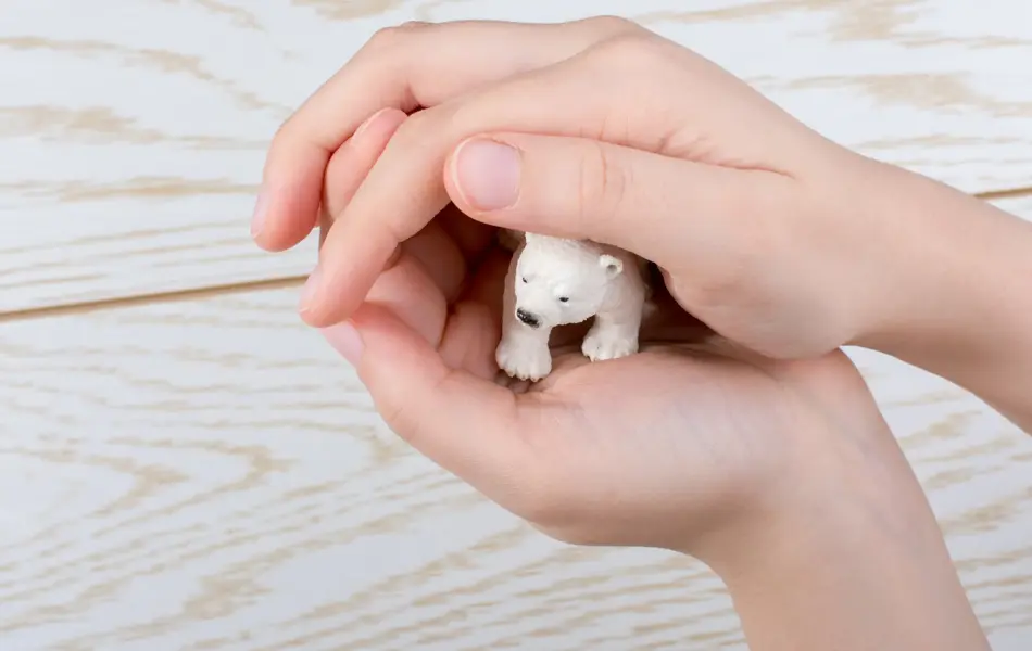 Hand holding a Polar bear model on a wooden background