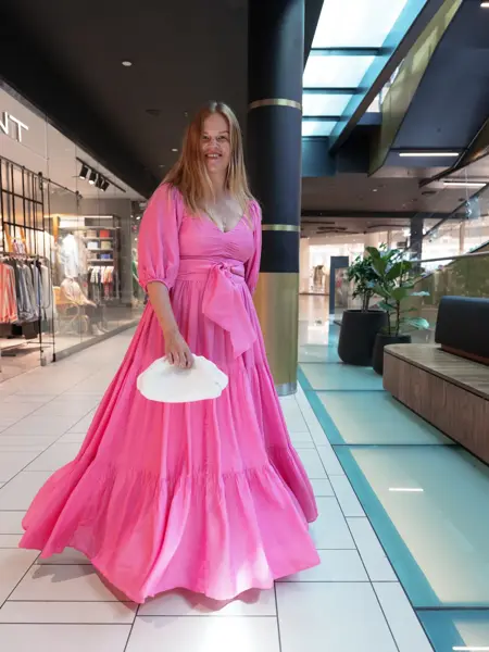 Damemodell med rosa lang kjole og liten hvit veske.