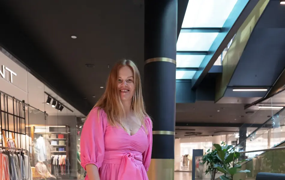 Damemodell med rosa lang kjole og liten hvit veske.