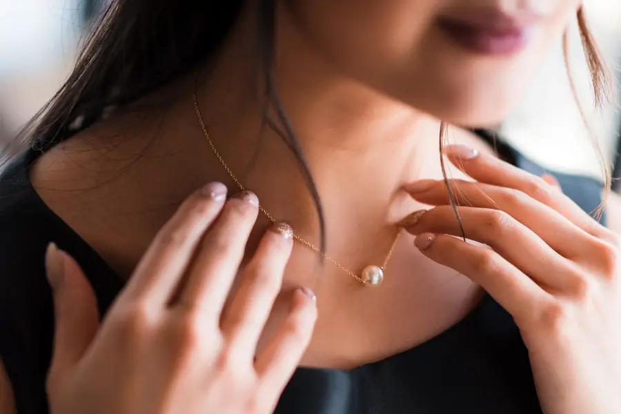 Young woman trying on neck an elegant pearl jewelry.Get dressed for the celebration