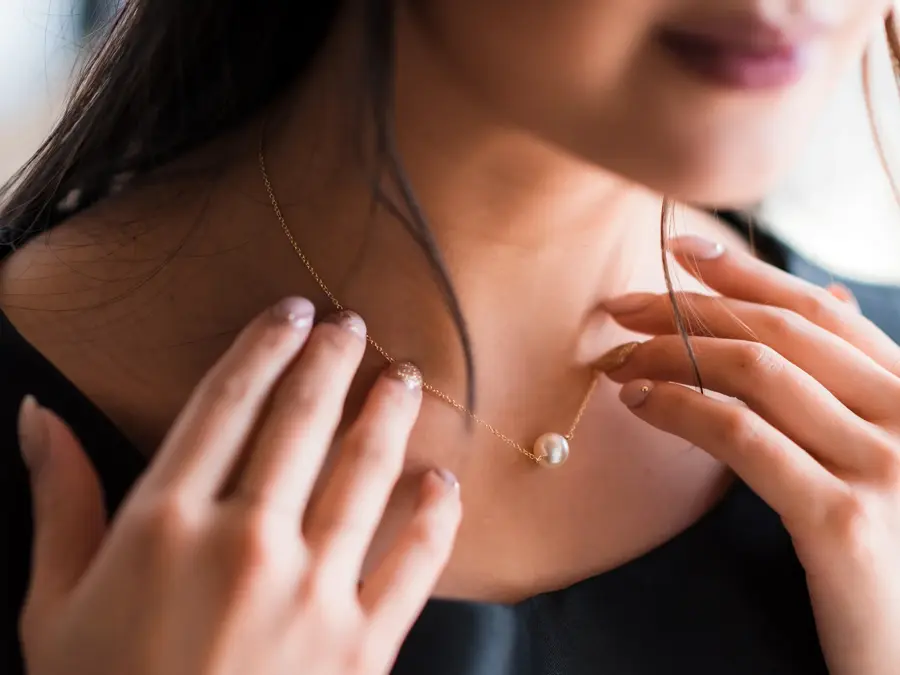 Young woman trying on neck an elegant pearl jewelry.Get dressed for the celebration