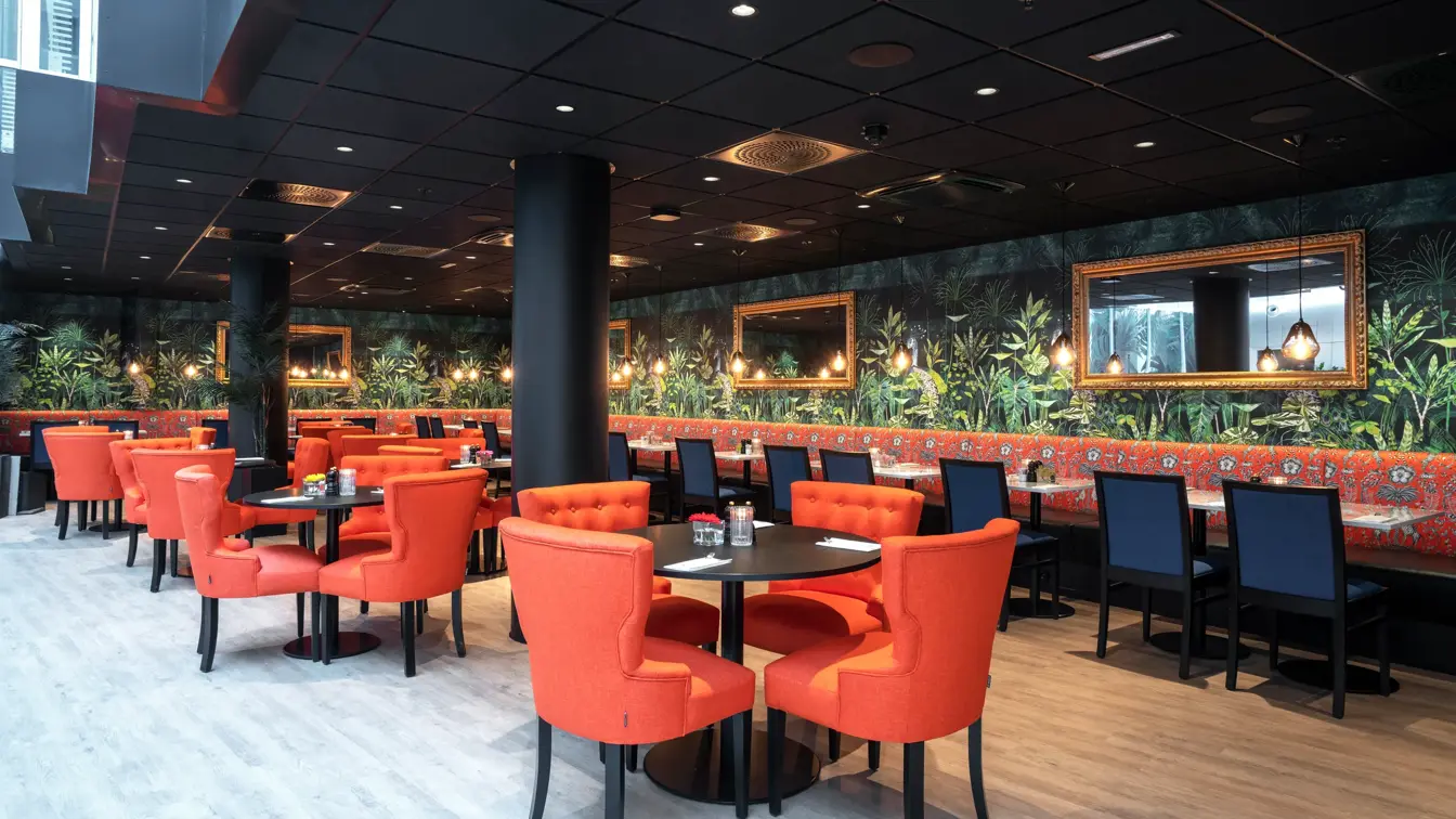 Oransje stoler, sorte runder bord og fargerik grønn tapet i restaurant på Thon Hotel Cecil