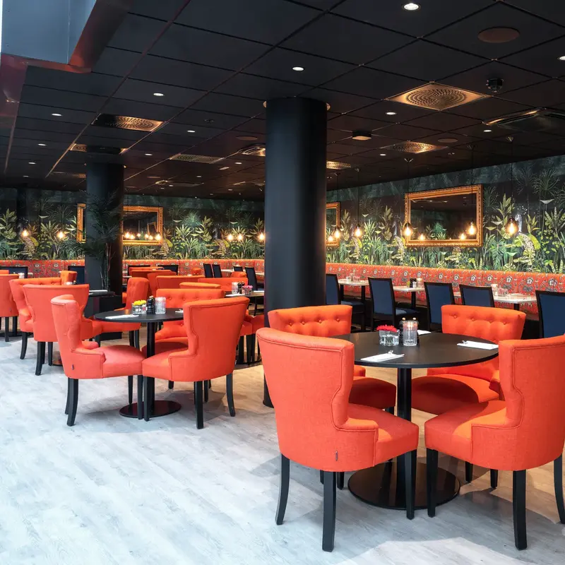 Oransje stoler, sorte runder bord og fargerik grønn tapet i restaurant på Thon Hotel Cecil