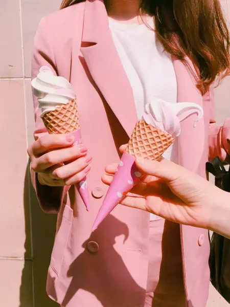 dame som har på seg rosa blazer og dressbukse med rosa neglelakk og iskrem i hånden