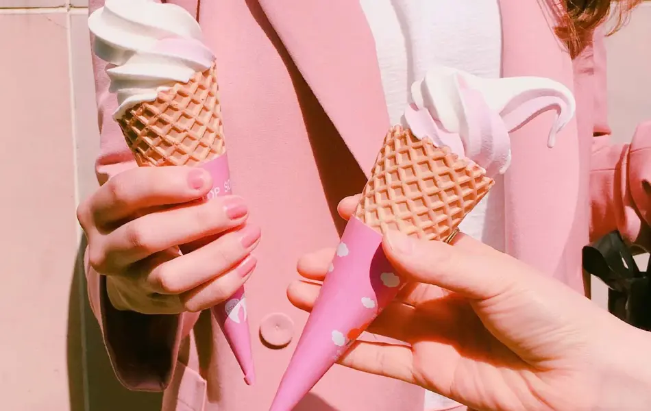 dame som har på seg rosa blazer og dressbukse med rosa neglelakk og iskrem i hånden