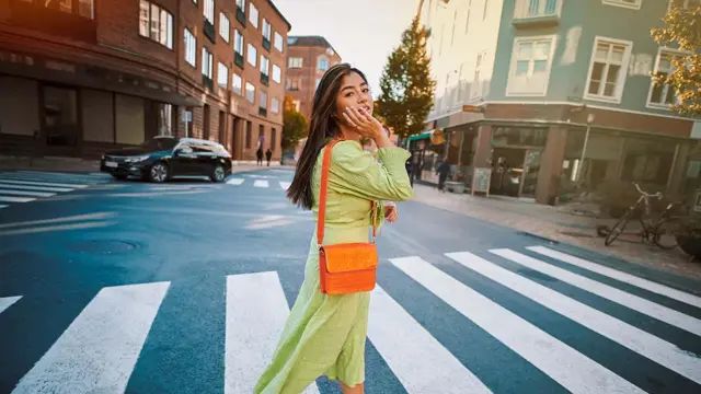 Jente med grønn kjole og oransje veske krysser gaten 