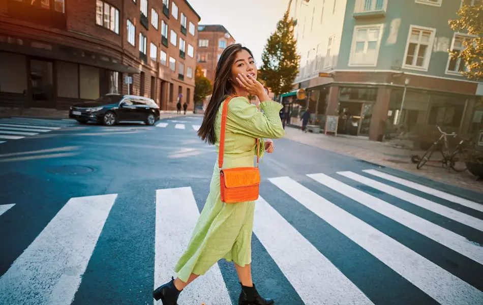 Jente med grønn kjole og oransje veske krysser gaten 