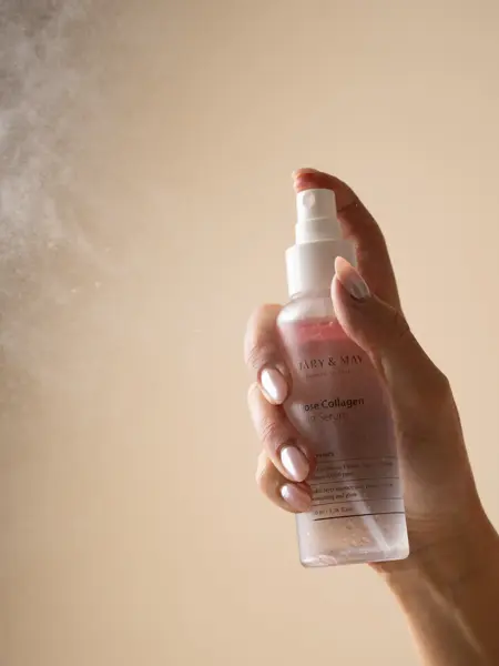 Hånd som holder en flaske med ansiktsmist og sprayer en dusj