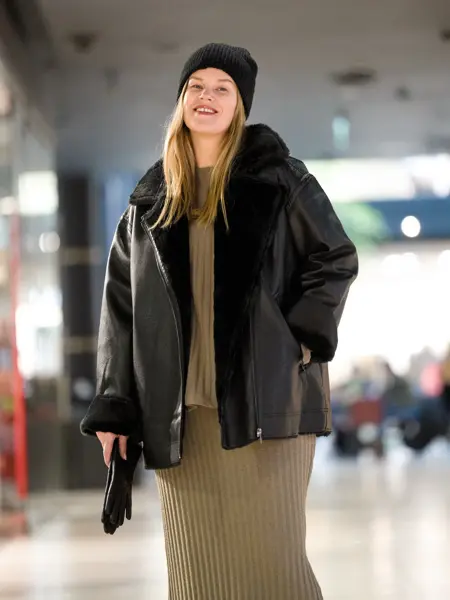 Dame i sort lue, sort skinnjakke med fuskepels, oliven grønn genser og skjørt.