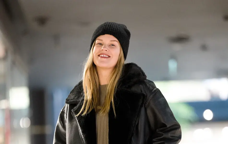 Dame i sort lue, sort skinnjakke med fuskepels, oliven grønn genser og skjørt.