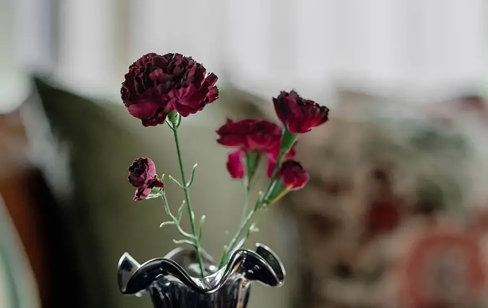 Vase med blomster og telysholdere på et brett som står på et bord. sofa med puter i bakgrunnen.