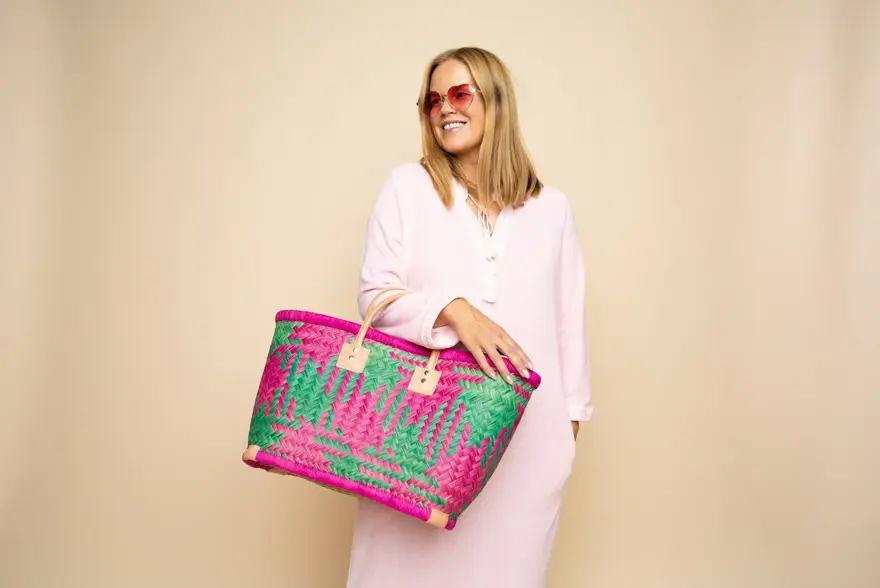 Damemodell i lyserosa lang kjole, rosa solbriller, stor flettet rosamønstret stråveske,