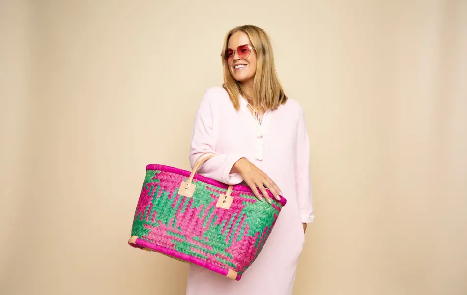 Damemodell i lyserosa lang kjole, rosa solbriller, stor flettet rosamønstret stråveske,