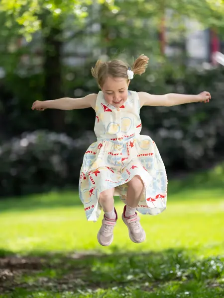 Jente hopper ute i mønstret kjole og rosa sneakers.