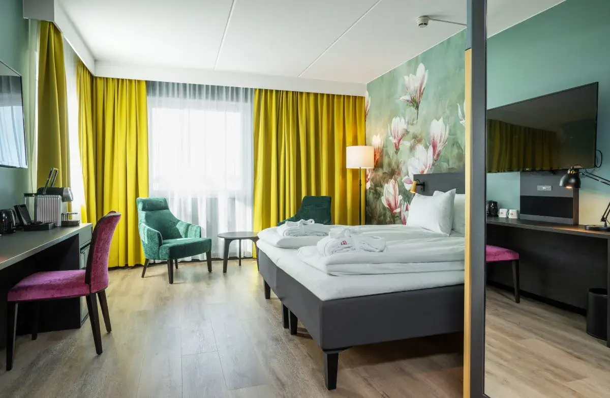 Hotellrom med sittegruppe foran gule gardiner som er trukket for vinduene. Foto.
