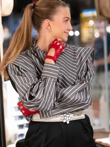 Ung kvinne med røde skinnhansker og stripete bluse står med hodet vendt til siden