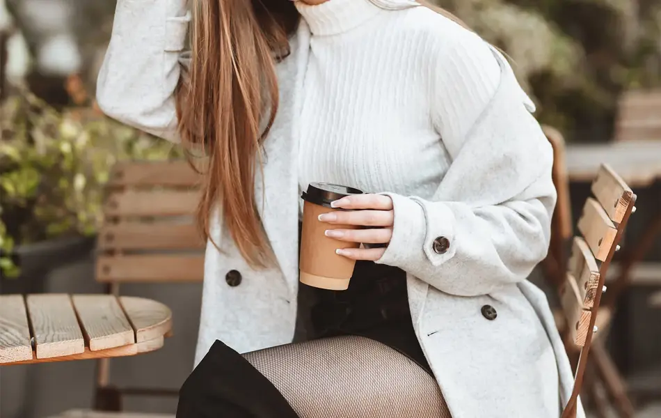 Jente med svarte, knelange støvletter og grå kåpe sitter på stol og smiler til kamera