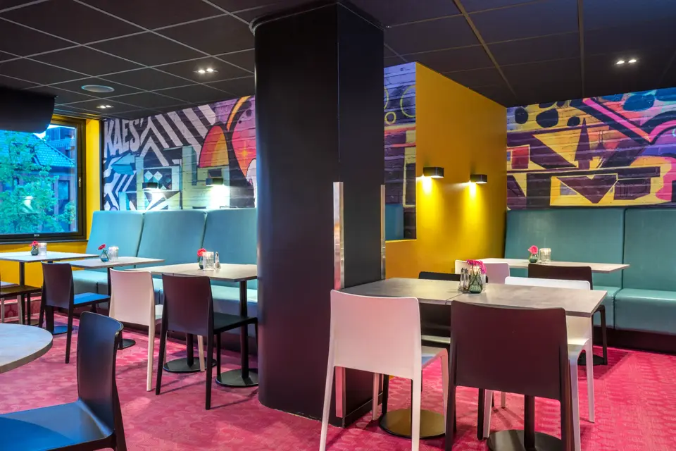 Frokostsalen hos Thon Hotel Trondheim. Veggene er malt med grafittiuttrykk, turkise sofaer, hvite og sorte stoler, spisebord, rosa gulvteppe.