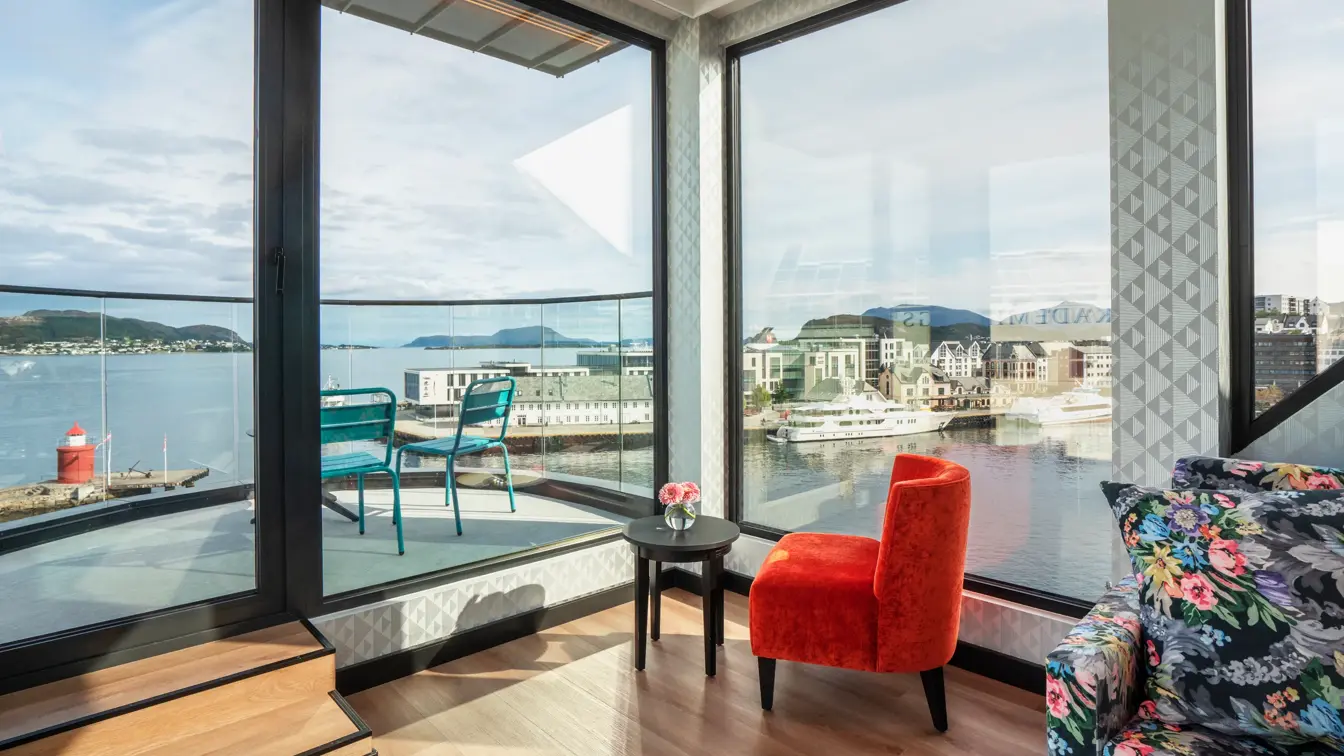 Panoramavindu med utsikt over vannet, salongbord, rød lenestol, balkong