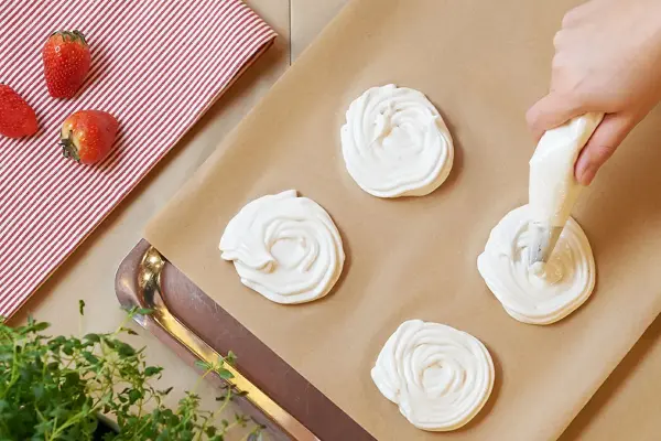 Noen som sprøyter marengs med sprøytepose på et brett