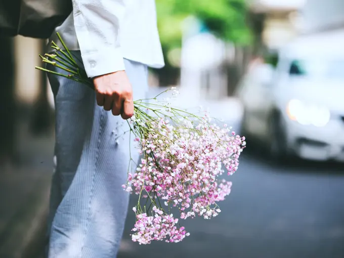 Nærbilde av hånd som holder en bukett blomster nedover låret, sett fra siden