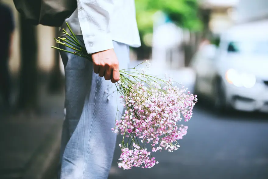Nærbilde av hånd som holder en bukett blomster nedover låret, sett fra siden
