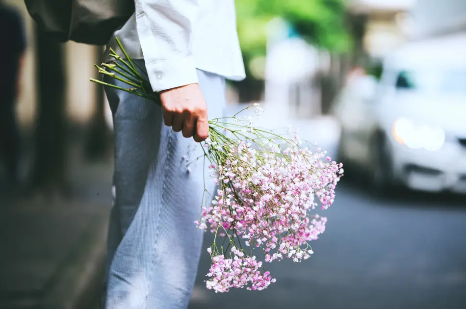 Nærbilde av hånd som holder en bukett blomster nedover låret, sett fra siden