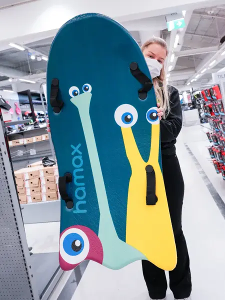 Jente med orangesekk og blådunjakke, og langrennski og slalåmski