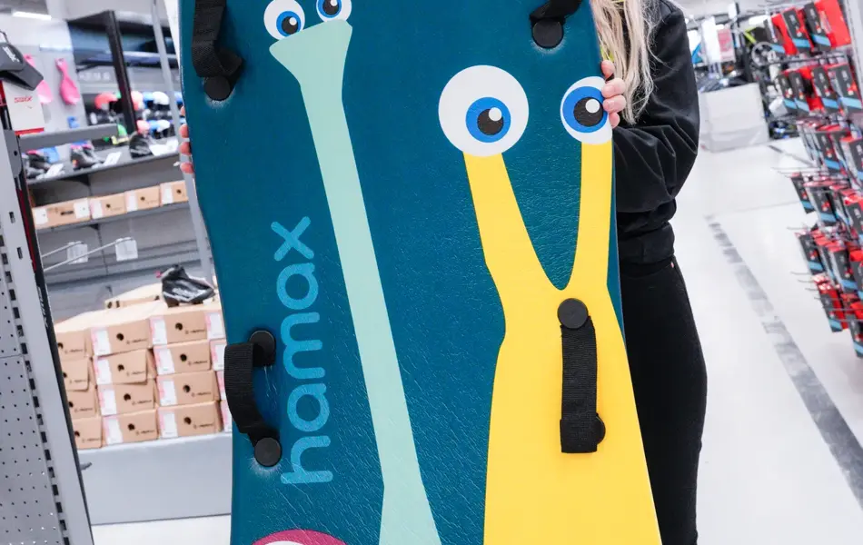 Jente med orangesekk og blådunjakke, og langrennski og slalåmski