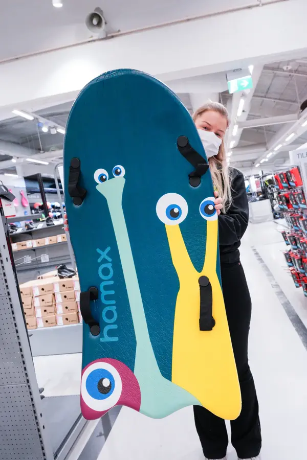 Jente med orangesekk og blådunjakke, og langrennski og slalåmski